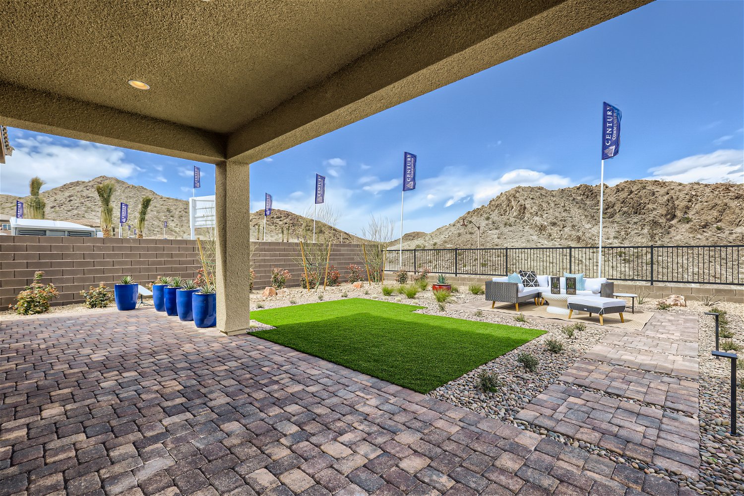 A brick patio with a brick walkway and a covered area with a fence and a hill in the.