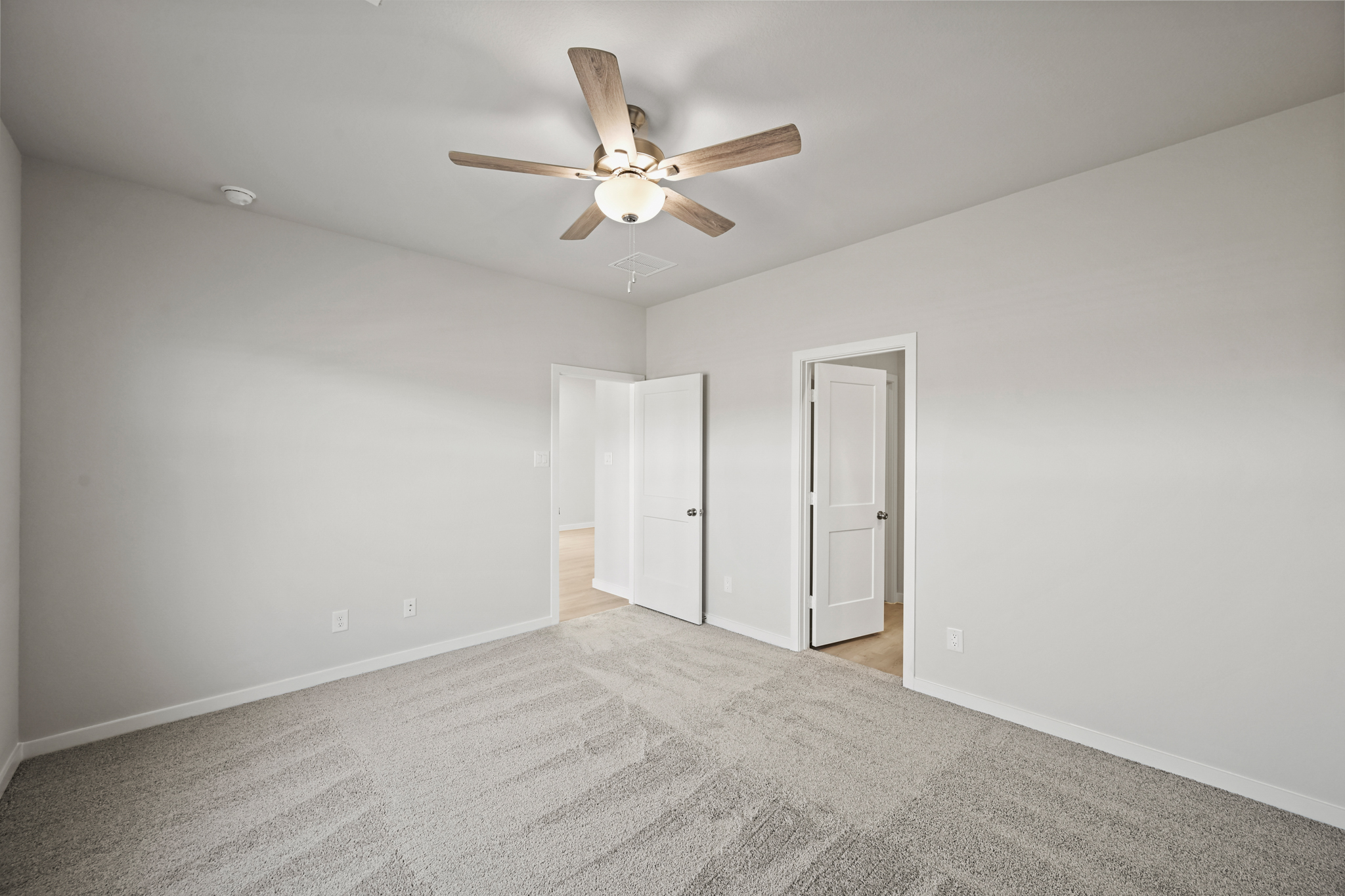 A room with a ceiling fan and a carpet.